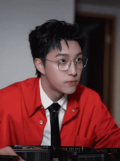 A Young Man Wearing Glasses And A Red Shirt Looks At Something GIF