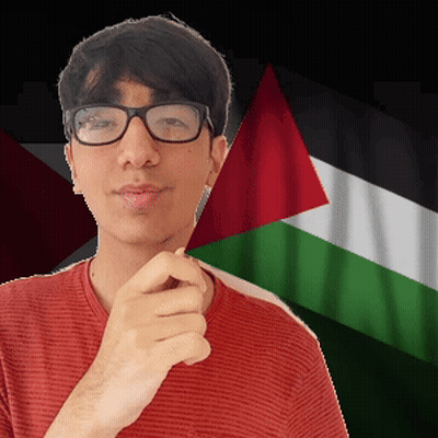 A Young Man Wearing Glasses And A Red Shirt Stands In Front Of A Flag GIF