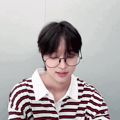 A Young Man Wearing Glasses And A Striped Shirt Looks Down GIF