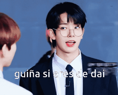 A Young Man Wearing Glasses And A Suit Is Talking To Another Man GIF