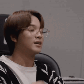 A Young Man Wearing Glasses And A Sweater Is Sitting In A Chair . GIF