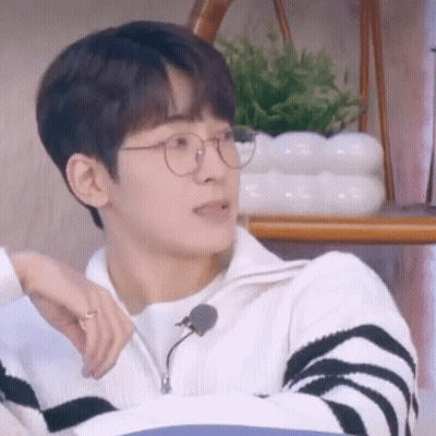 A Young Man Wearing Glasses And A Sweater Is Sitting On A Couch . GIF