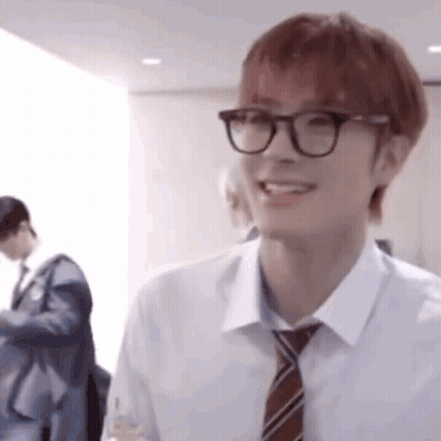 A Young Man Wearing Glasses And A Tie Is Smiling And Looking At The Camera . GIF