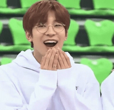 A Young Man Wearing Glasses And A White Hoodie Is Laughing With His Hands On His Face . GIF