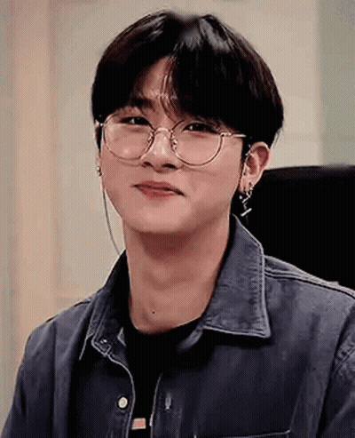 A Young Man Wearing Glasses And Earrings Is Smiling . GIF