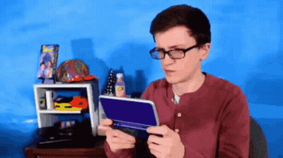 A Young Man Wearing Glasses Is Holding A Nintendo 3Ds GIF