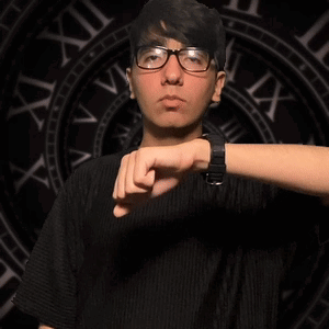 A Young Man Wearing Glasses Is Pointing At His Watch In Front Of A Clock That Says Viii On It GIF