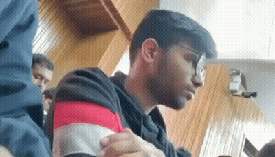 A Young Man Wearing Glasses Is Sitting At A Table In A Room . GIF
