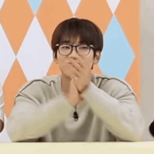 A Young Man Wearing Glasses Is Sitting At A Table With His Hands Folded In Front Of His Face . GIF
