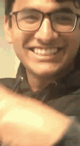 A Young Man Wearing Glasses Is Smiling And Making A Peace Sign . GIF