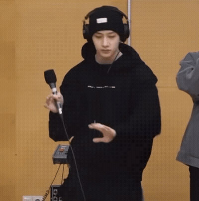 A Young Man Wearing Headphones And A Beanie Is Holding A Microphone And Dancing . GIF