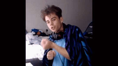A Young Man Wearing Headphones And A Blue And Purple Blanket Is Sitting On A Bed . GIF