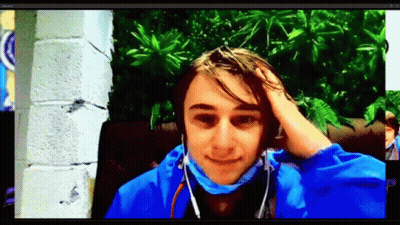 A Young Man Wearing Headphones And A Blue Jacket Holds His Hand To His Forehead GIF
