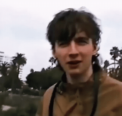 A Young Man Wearing Headphones And A Camera Is Standing In Front Of Palm Trees . GIF