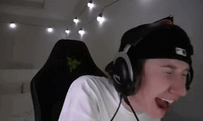 A Young Man Wearing Headphones And A Hat Is Sitting In A Chair . GIF