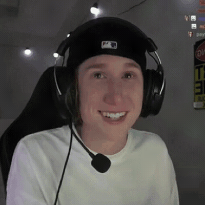 A Young Man Wearing Headphones And A Hat Is Smiling While Sitting In A Chair . GIF