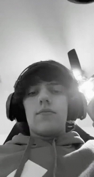 A Young Man Wearing Headphones And A Hoodie Is Taking A Selfie . GIF