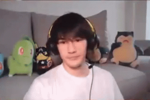 A Young Man Wearing Headphones And A Microphone Is Sitting On A Couch . GIF