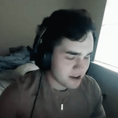 A Young Man Wearing Headphones And A Necklace Is Sitting In Front Of A Window . GIF