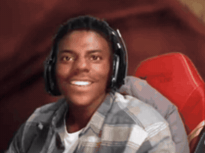 A Young Man Wearing Headphones And A Plaid Shirt Smiles For The Camera GIF