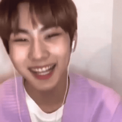 A Young Man Wearing Headphones And A Purple Shirt Is Smiling And Looking At The Camera . GIF