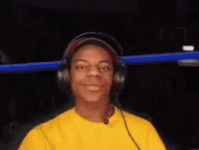 A Young Man Wearing Headphones And A Yellow Shirt Is Looking At The Camera . GIF