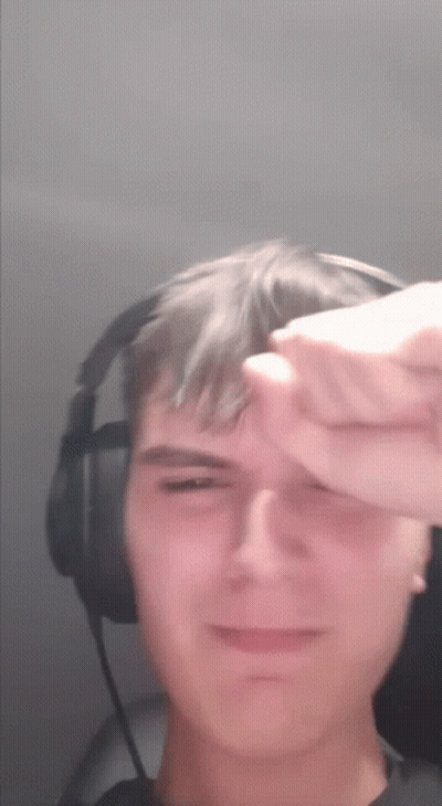 A Young Man Wearing Headphones Is Covering His Face With His Hand GIF