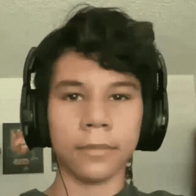 A Young Man Wearing Headphones Is Looking At The Camera In A Living Room . GIF