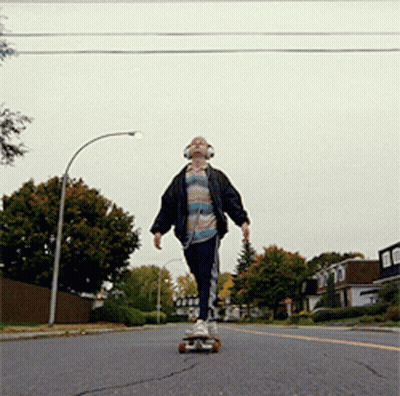 A Young Man Wearing Headphones Is Riding A Skateboard Down A Street GIF