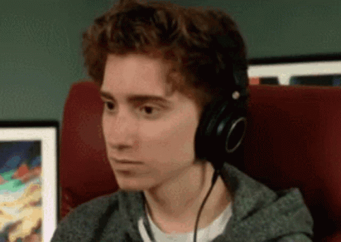 A Young Man Wearing Headphones Is Sitting In A Chair Looking At Something . GIF
