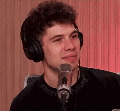 A Young Man Wearing Headphones Is Sitting In Front Of A Microphone And Smiling . GIF