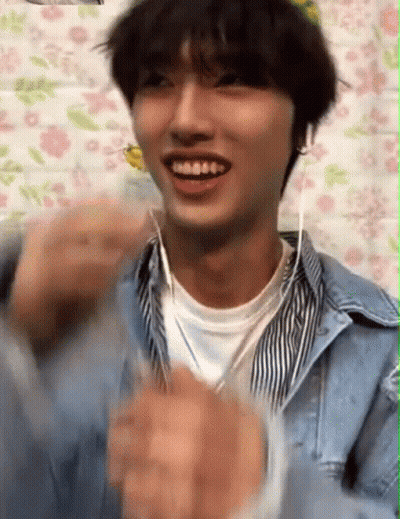 A Young Man Wearing Headphones Is Smiling And Clapping His Hands . GIF