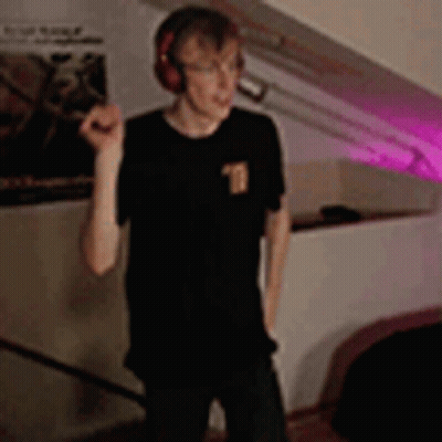 A Young Man Wearing Headphones Is Standing In A Room . GIF
