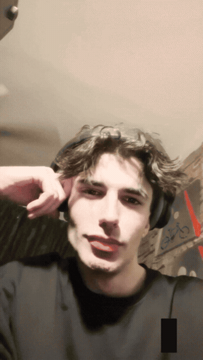A Young Man Wearing Headphones Looks At The Camera With A Picture Of The Eiffel Tower In The Background GIF