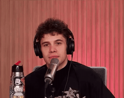 A Young Man Wearing Headphones Stands In Front Of A Microphone With A Sticker On His Shirt That Says Ozzy GIF