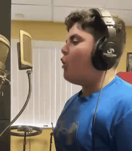 A Young Man Wearing Headphones With The Letter S On Them Sings Into A Microphone GIF