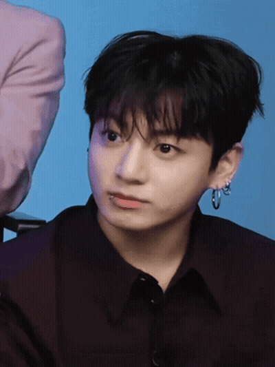 A Young Man Wearing Hoop Earrings And A Black Shirt Looks At The Camera GIF