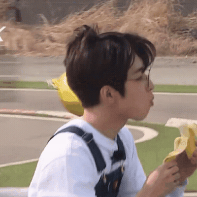 A Young Man Wearing Overalls Is Eating A Banana GIF