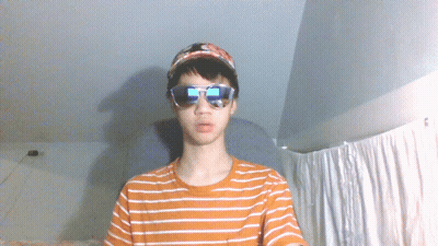 A Young Man Wearing Sunglasses And A Baseball Cap Looks At The Camera GIF