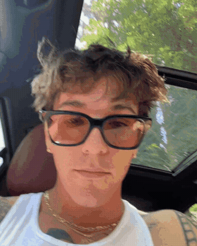 A Young Man Wearing Sunglasses And A White Tank Top Is Sitting In A Car GIF