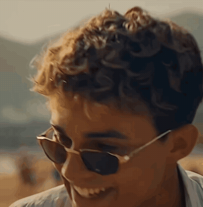 A Young Man Wearing Sunglasses Is Smiling And Looking At The Camera GIF