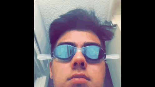 A Young Man Wearing Swimming Goggles With A Toothbrush Attached To His Ear GIF