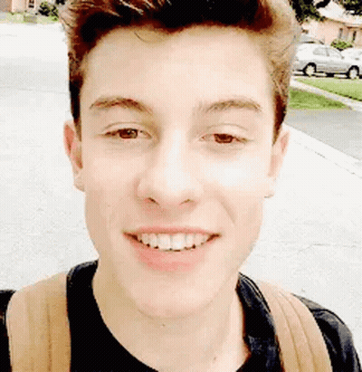 A Young Man With A Backpack Is Smiling For The Camera While Walking Down The Street . GIF