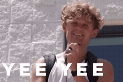 A Young Man With A Backpack Is Smiling In Front Of A Brick Wall With Yee Yee Written In White Letters GIF