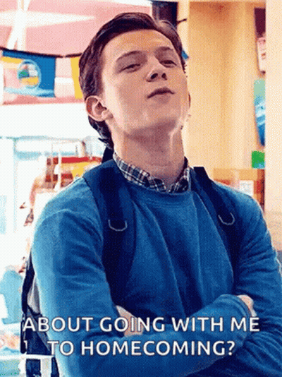 A Young Man With A Backpack Is Standing In A Room With His Arms Crossed And Talking About Going With Me To Homecoming . GIF