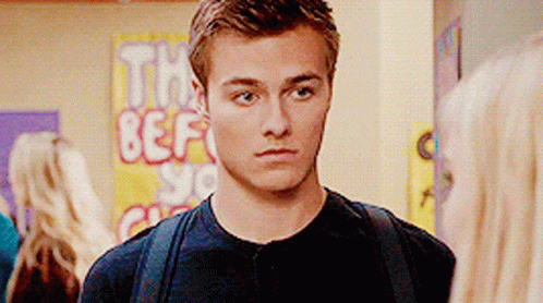 A Young Man With A Backpack Stands In Front Of A Sign That Says The Best GIF
