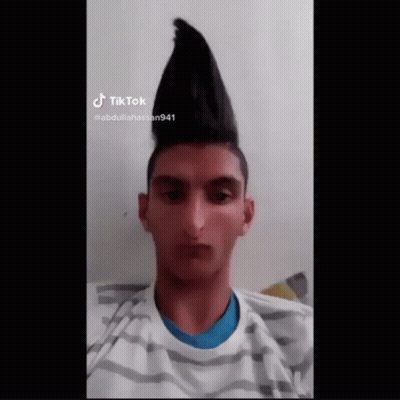 A Young Man With A Mohawk Hairstyle Is Wearing A Striped Shirt And Looking At The Camera . GIF