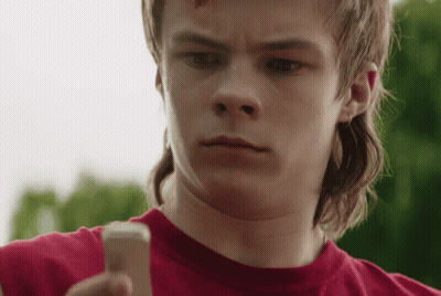 A Young Man With A Mullet Is Holding A Cell Phone . GIF