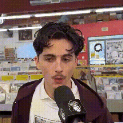A Young Man With A Mustache Is Talking Into A Microphone . GIF
