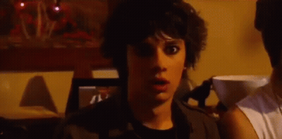 A Young Man With A Surprised Look On His Face Is Standing In A Dark Room . GIF